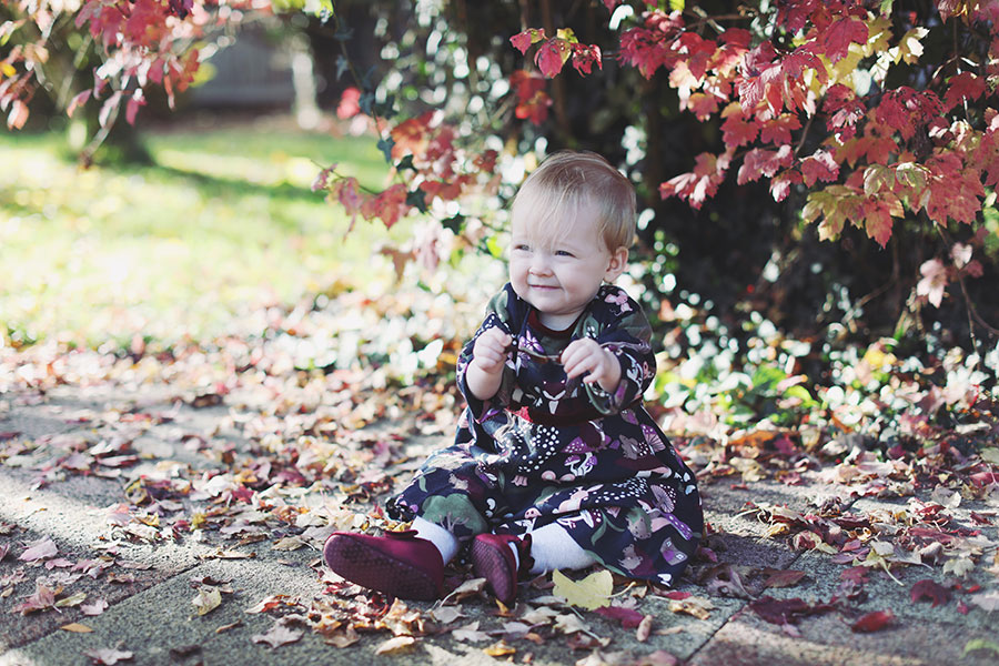 Baby in cosy dress surrounded by orange autumn leaves during outdoor birthday shoot in Derbyshire