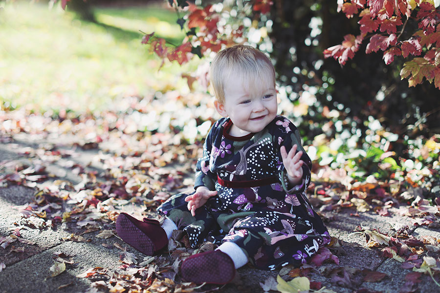 Baby in cosy dress surrounded by orange autumn leaves during outdoor birthday shoot in Derbyshire
