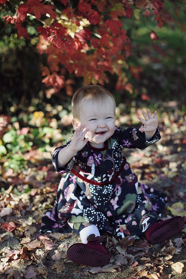 Baby in cosy dress surrounded by orange autumn leaves during outdoor birthday shoot in Derbyshire