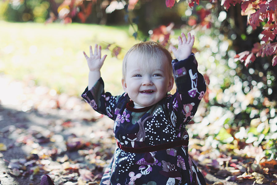 Baby in cosy dress surrounded by orange autumn leaves during outdoor birthday shoot in Derbyshire