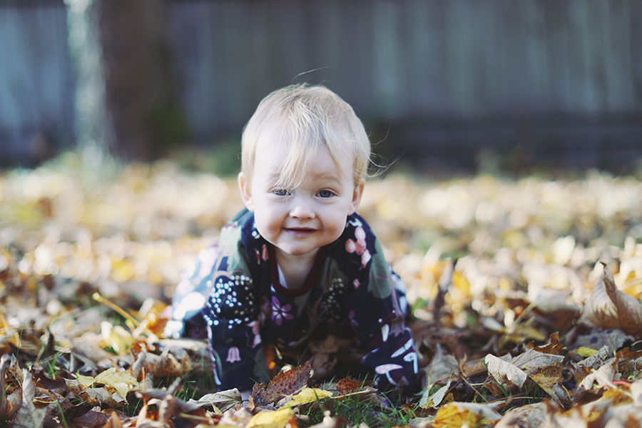 Baby in cosy dress surrounded by orange autumn leaves during outdoor birthday shoot in Derbyshire