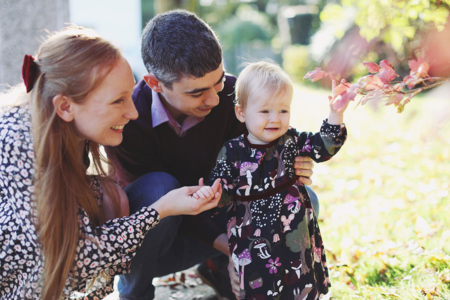Baby in cosy dress surrounded by orange autumn leaves during outdoor birthday shoot in Derbyshire