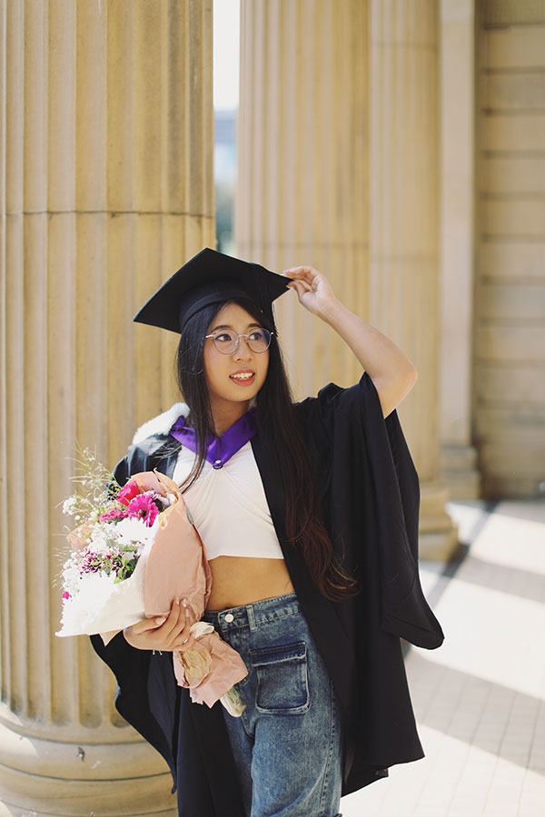 Smiling Sheffield University graduate in black gown holding hat