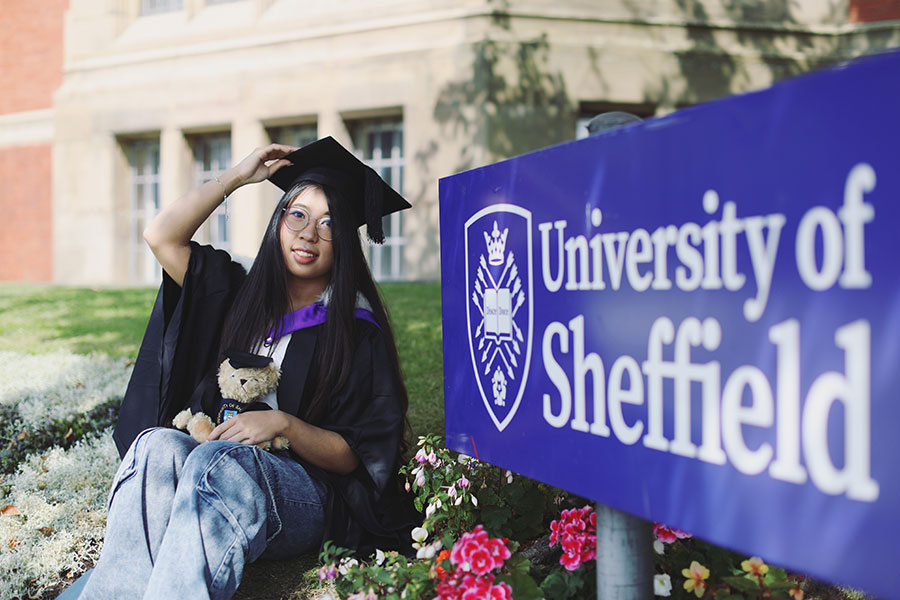 Smiling Sheffield University graduate in black gown holding hat