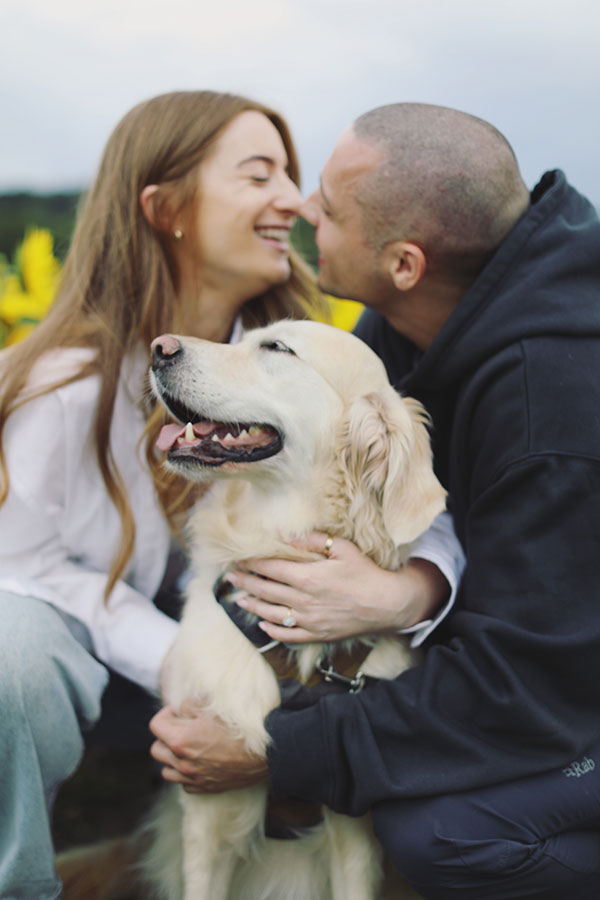 Ellie and Kamen posing in a sunflower field with their dog during engagement session