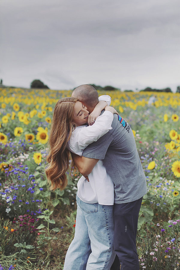 Ellie and Kamen posing in a sunflower field with their dog during engagement session