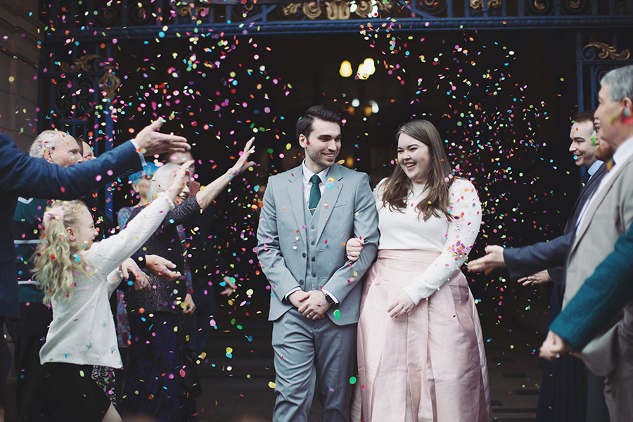 Newly married couple walking down the steps of Sheffield Town Hall as guests throw confetti