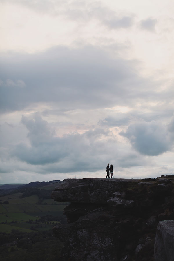 Diana & Alex ♡ Peak District Engagement Photoshoot 2 Diana and Alex standing close together in the Peak District, surrounded by green hills and ferns under an overcast sky.