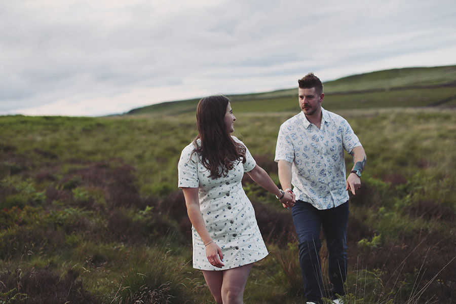Diana & Alex ♡ Peak District Engagement Photoshoot 3 Diana and Alex standing close together in the Peak District, surrounded by green hills and ferns under an overcast sky.