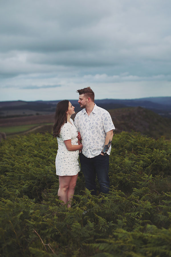 Diana & Alex ♡ Peak District Engagement Photoshoot 14 Diana and Alex holding hands on a hillside in the Peak District, with rolling countryside in the background.