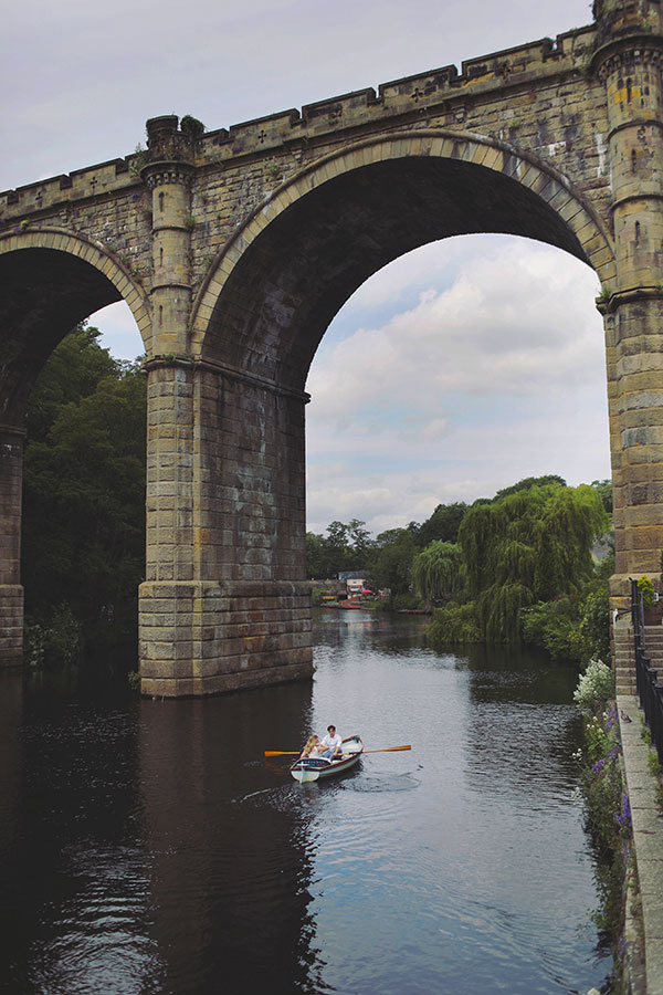 Couple rowing a boat on the River Nidd during a sunny Knaresborough engagement photoshoot.