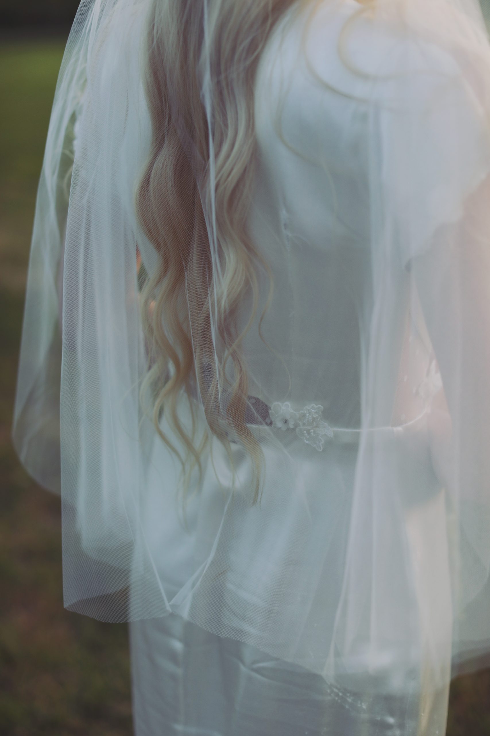 Ethereal bride in a lace wedding gown standing among blooming spring flowers at golden hour