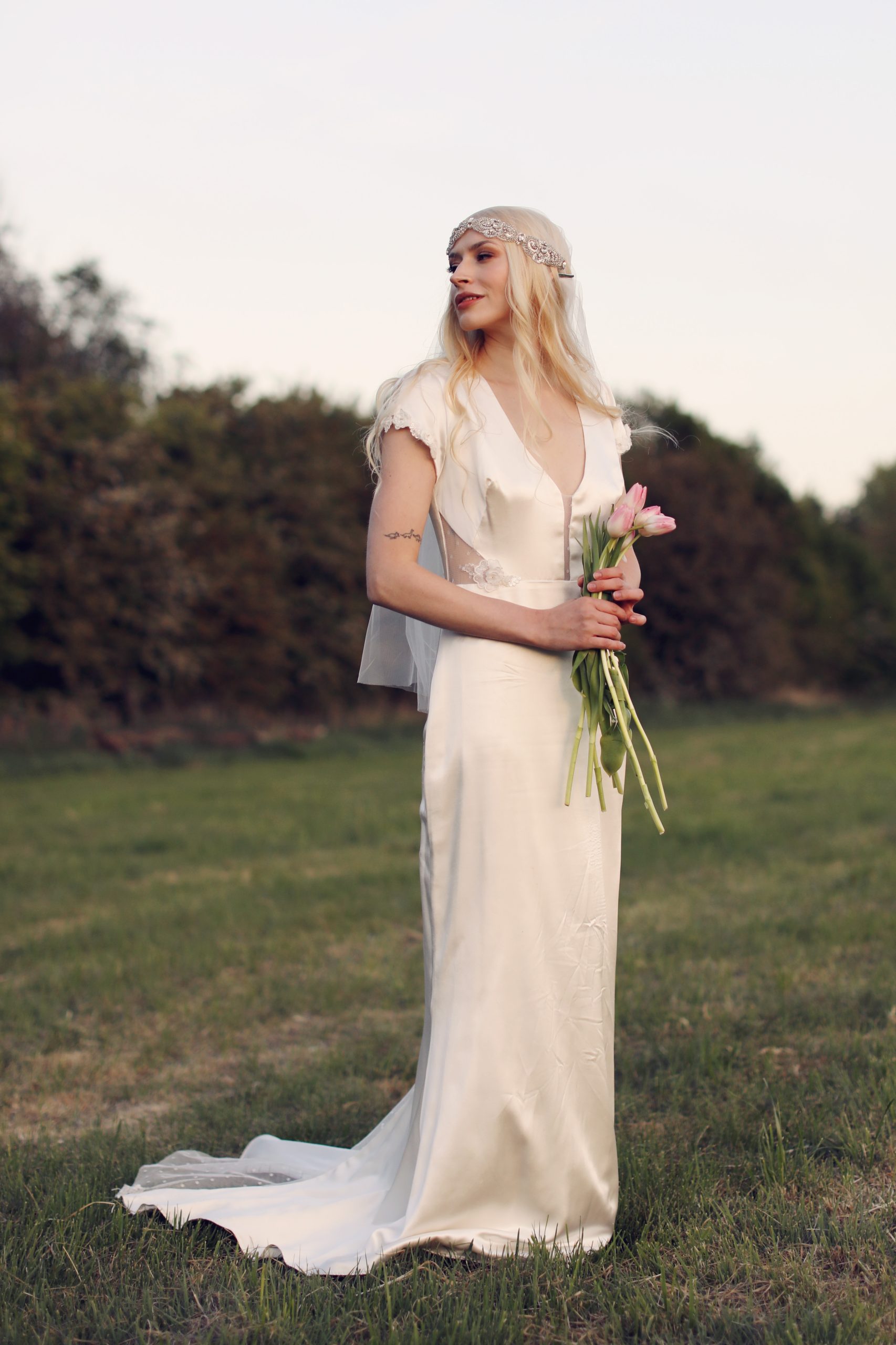 Ethereal bride in a lace wedding gown standing among blooming spring flowers at golden hour
