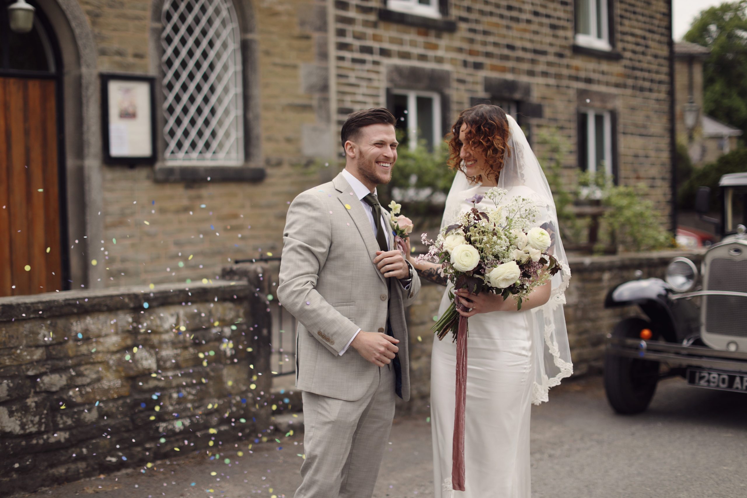 Bride and groom standing beside a vintage wedding car from Peak Wedding Hire.