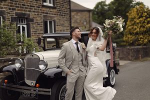 Bride laughing with groom outside a traditional Yorkshire stone house.