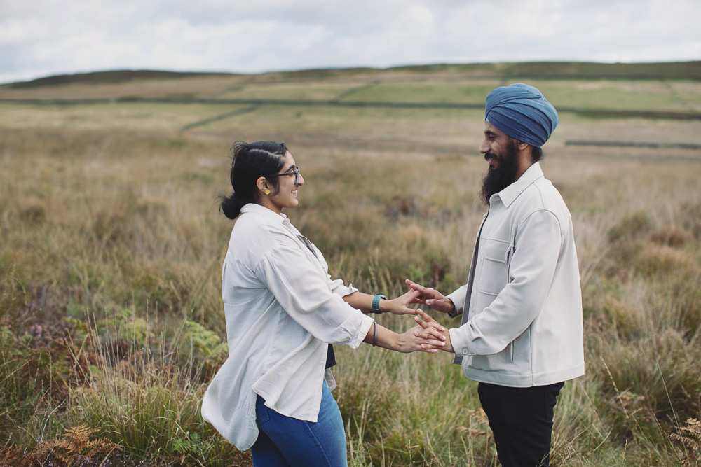 Couple holding hands during their Peak District proposal photoshoot with views across the countryside