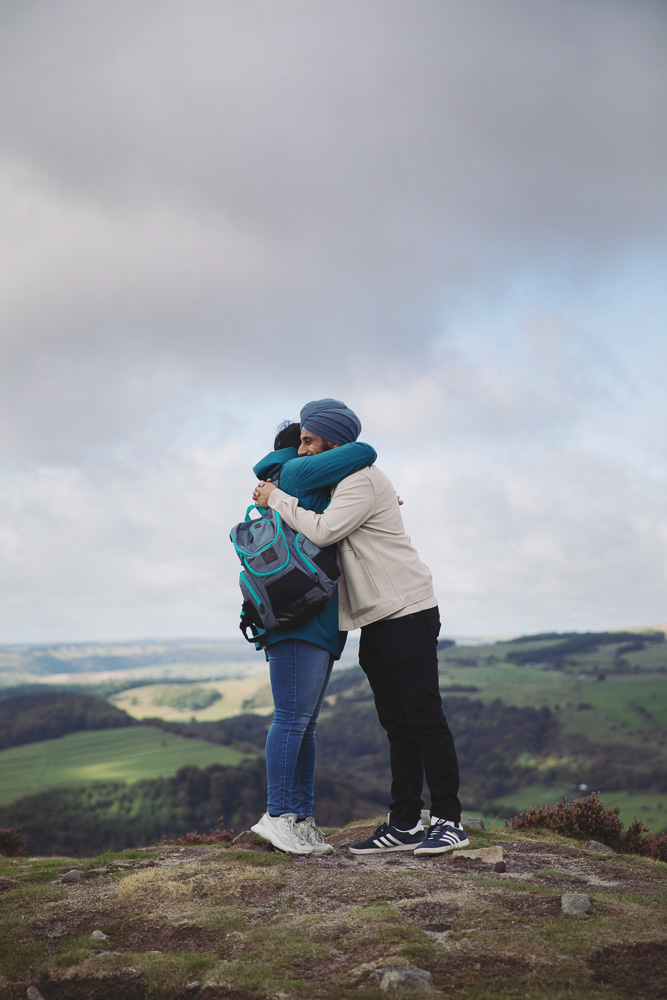 Couple embracing against the dramatic skies and countryside of the Peak District